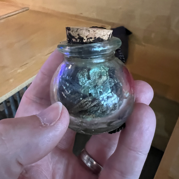 A glass jar with a dislodged cork lid, containing two graduation tassels from high school & college